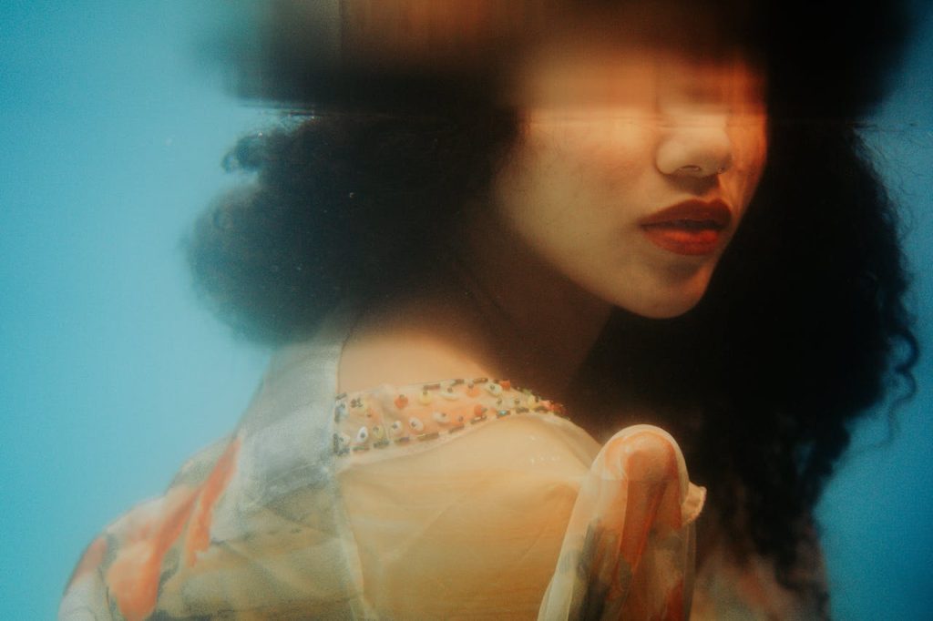 Artistic portrait of a woman with wavy hair against a blurred blue background, showcasing creativity.